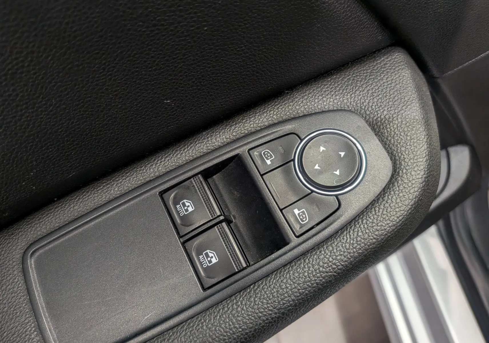 Gros plan sur les commandes de lève-vitres et réglage des rétroviseurs côté gauche d’une Renault Clio V gris platine.