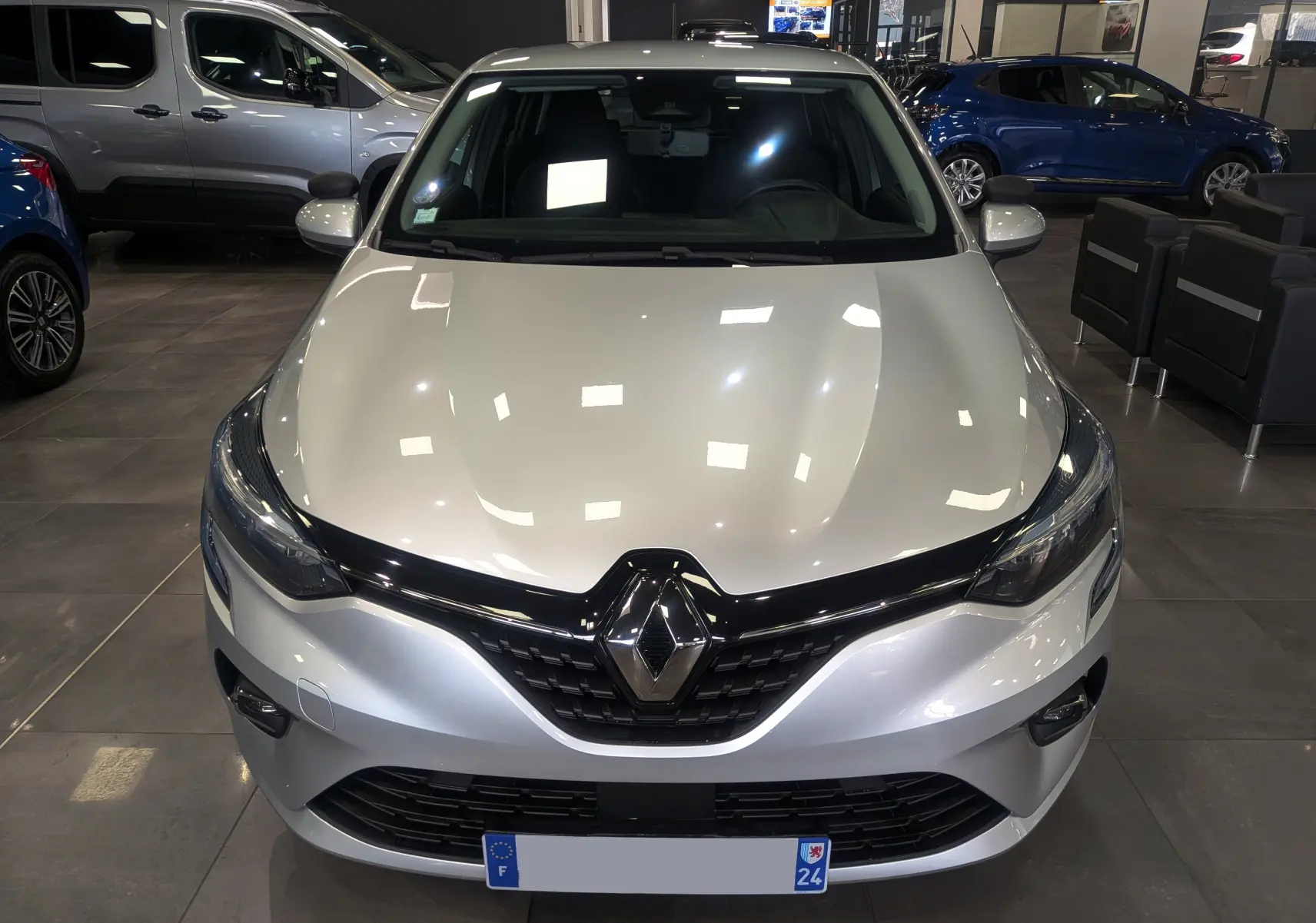 Vue avant d'une Renault Clio V TCe 90 Gris Platine en showroom, mettant en valeur sa calandre noire et ses phares LED.