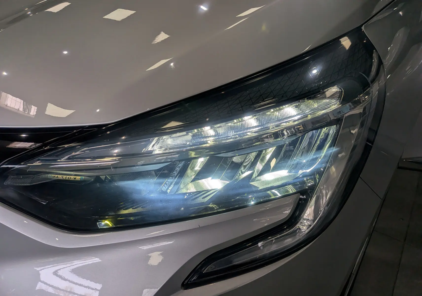 Gros plan sur le phare avant droit allumé d'une Renault Clio V gris platine, mettant en valeur ses LED modernes.