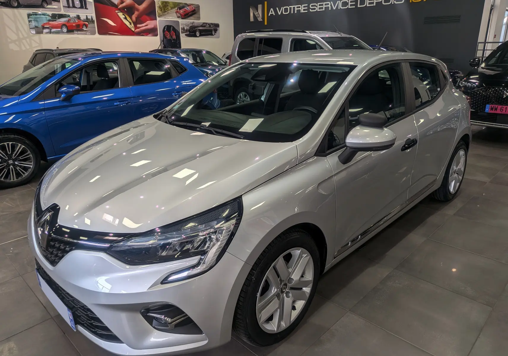 Renault Clio V gris platine vue 3/4 avant droit en intérieur, avec phares LED et jantes alliage visibles.