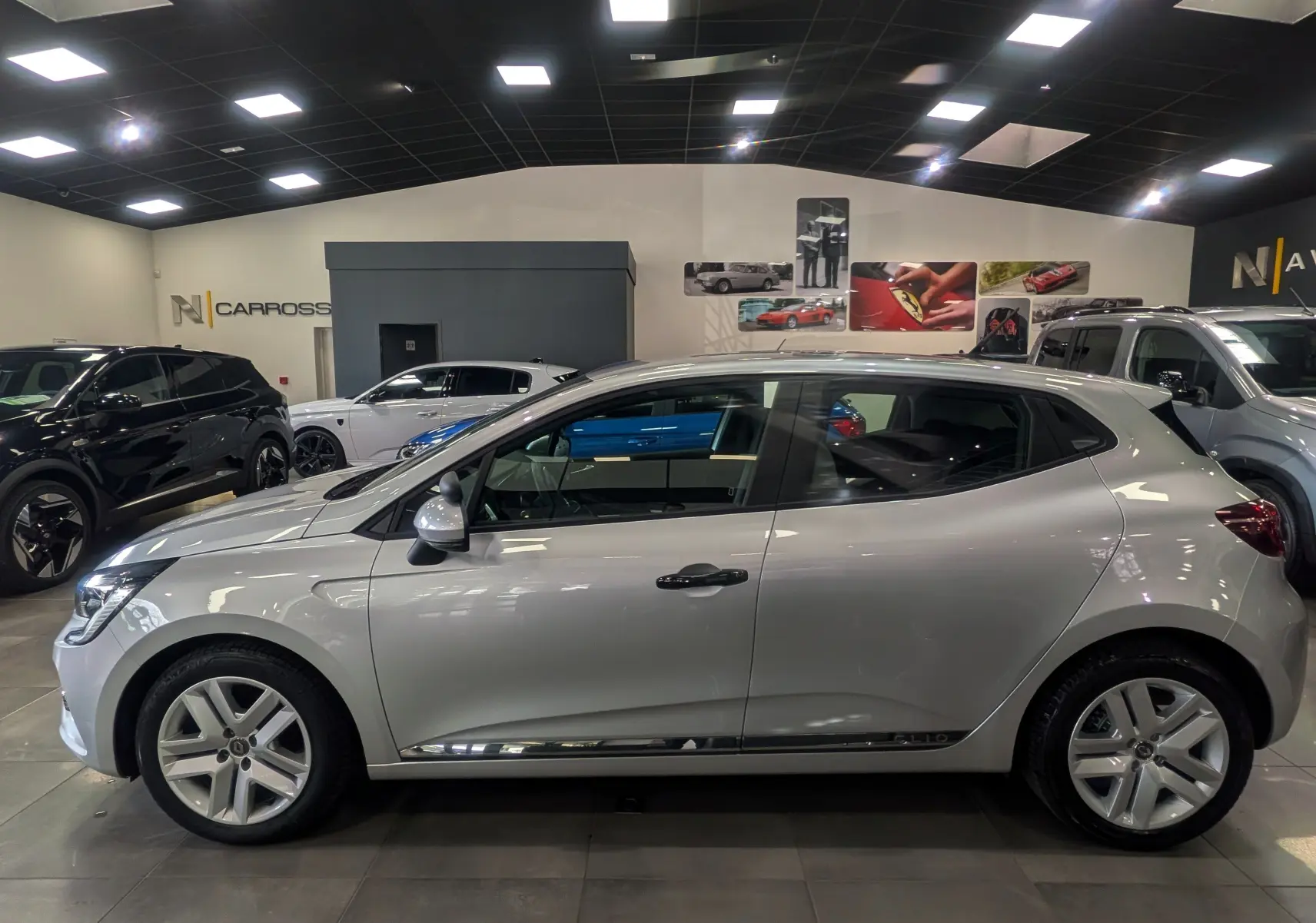 Vue latérale droite d'une Renault Clio V gris platine en intérieur, avec jantes alliage et poignées noires.