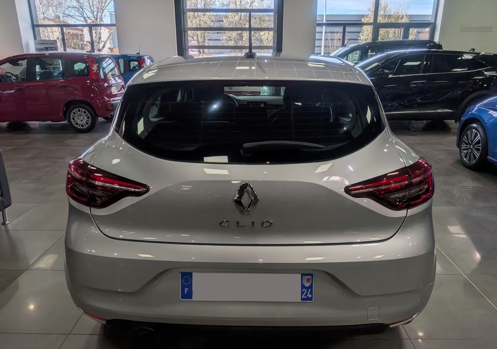 Vue arrière d'une Renault Clio V gris platine 2021 en showroom, avec feux arrière LED et logo central visible.