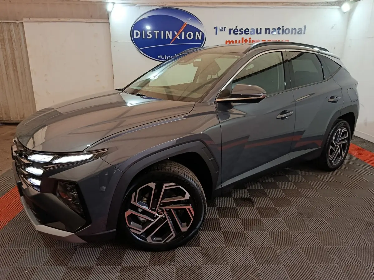Vue 3/4 avant droit du Hyundai Tucson 1.6 Hybrid gris foncé avec jantes au design géométrique et feux LED allumés.