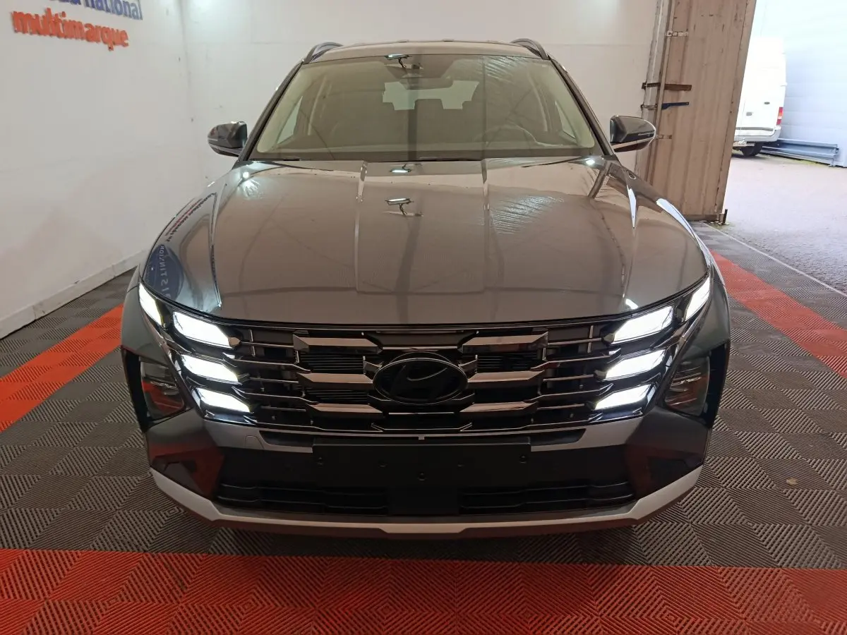 Vue avant d’un Hyundai Tucson gris foncé 2025 avec calandre chromée et feux LED allumés dans un garage.