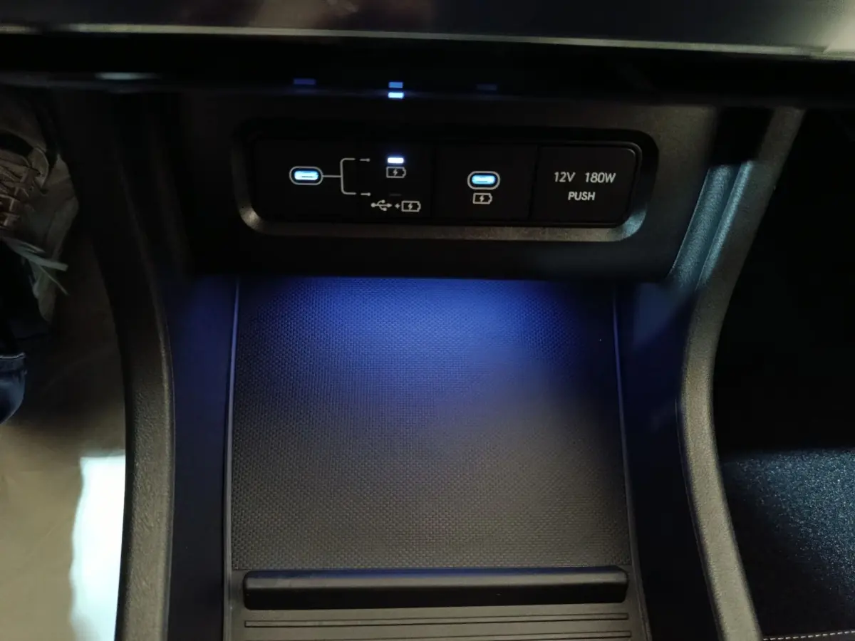 Vue rapprochée de la zone de recharge sans fil et ports USB éclairés en bleu dans l’habitacle du Hyundai Tucson gris foncé 2025.