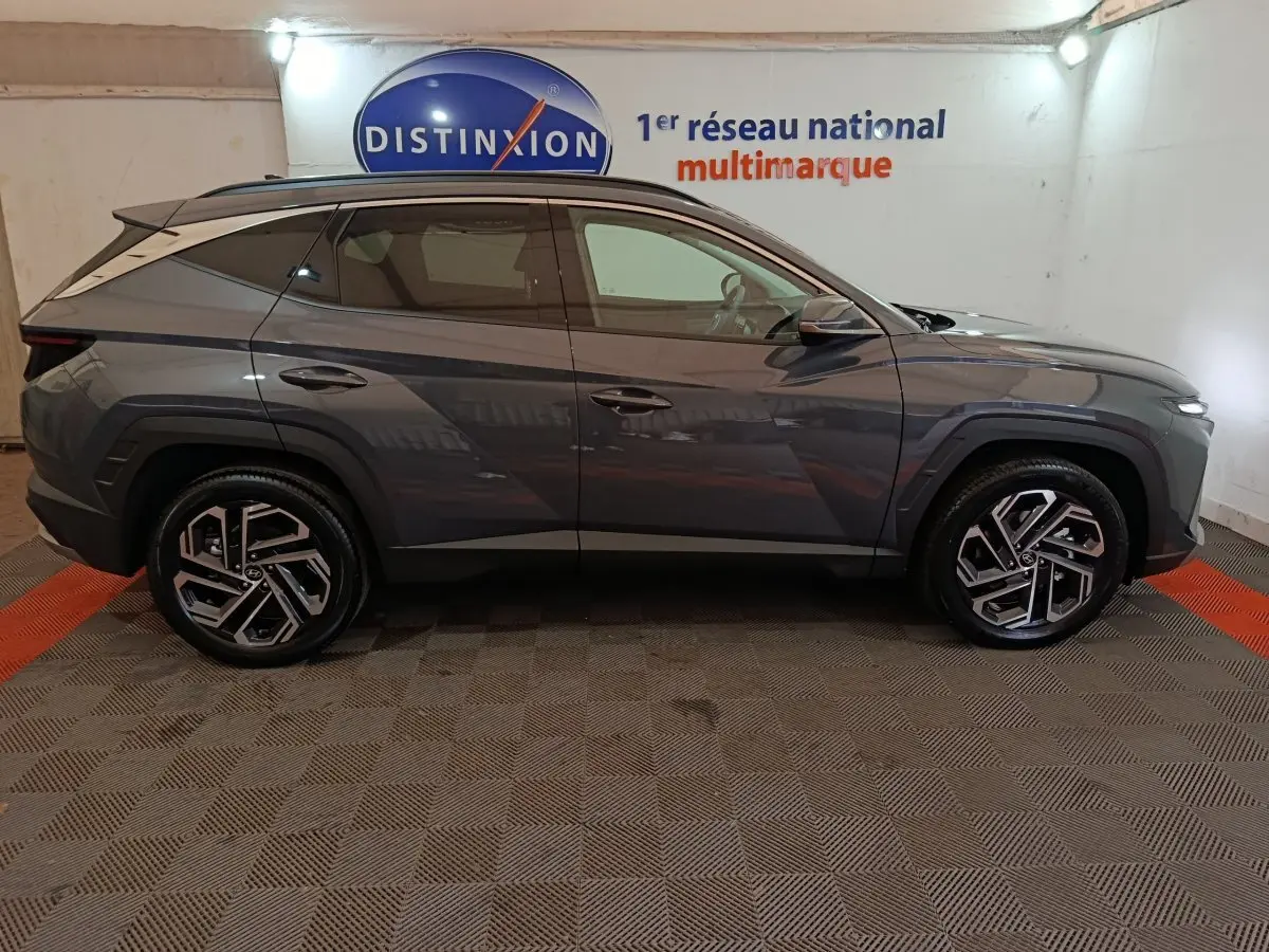 Vue de profil côté gauche d'un Hyundai Tucson gris foncé avec jantes alliage au design moderne, en intérieur showroom.