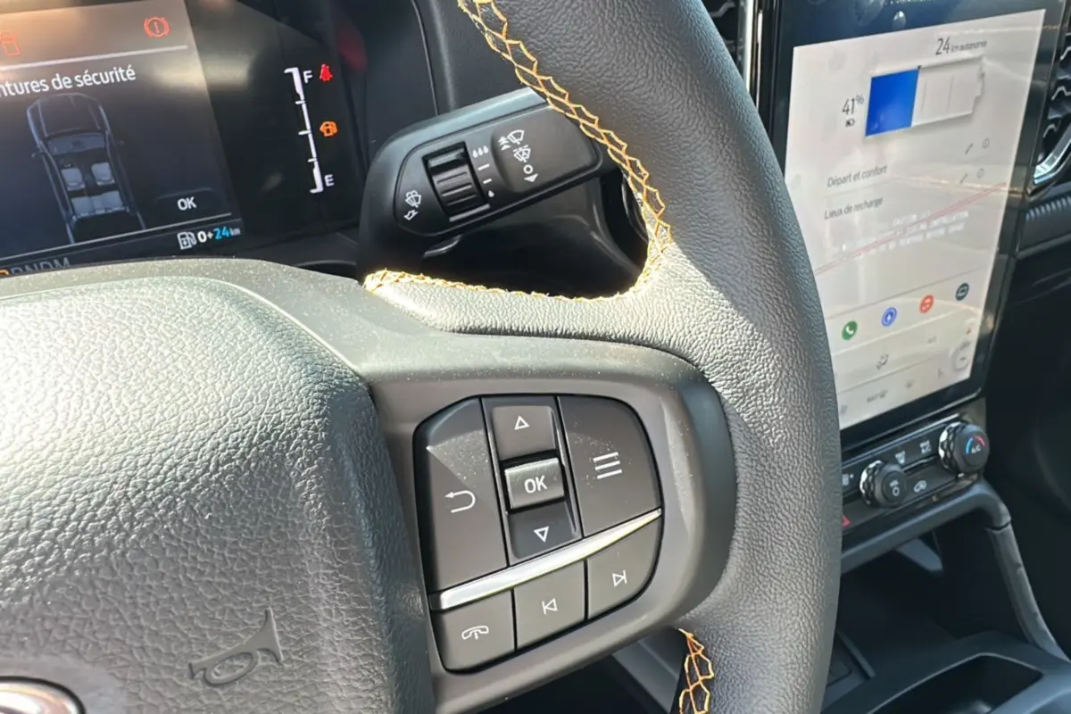 Gros plan sur le volant cuir noir avec surpiqûres jaunes du Ford Ranger 2026, écran tactile et commandes au volant visibles.