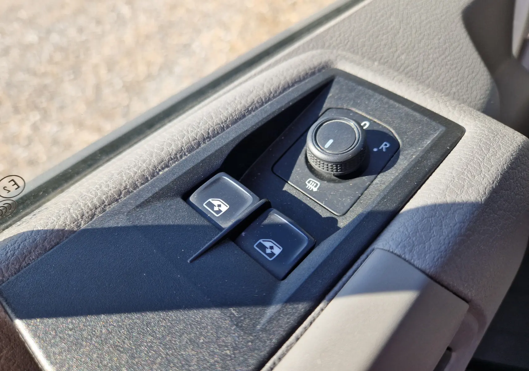 Gros plan sur les commandes de réglage des rétroviseurs et vitres électriques côté conducteur d’un Volkswagen Crafter blanc.