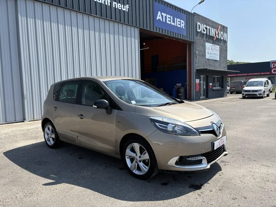 Renault Scénic III beige vue 3/4 avant droit, jantes aluminium, stationné devant un atelier automobile.