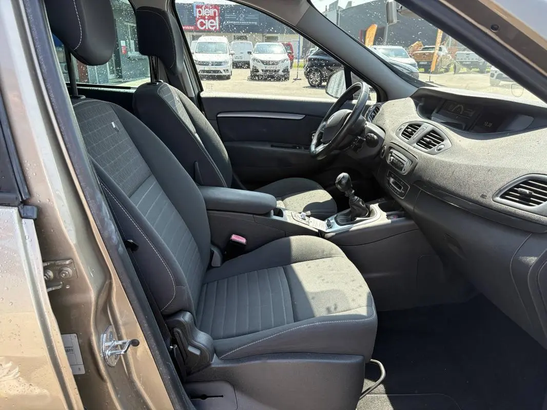 Vue intérieure côté conducteur du Renault Scénic beige, montrant sièges tissu, volant cuir et console centrale avec boîte manuelle.