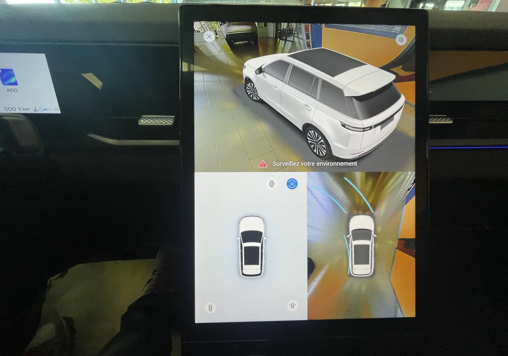 Écran intérieur montrant la vue 3D et aérienne d’un JAECOO J5 gris Phantom avec toit noir dans un garage.