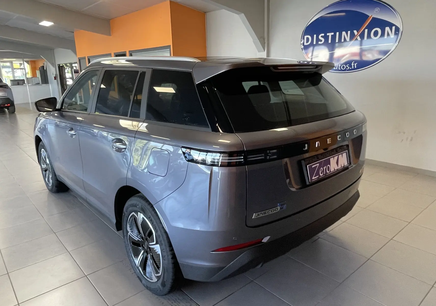 Vue 3/4 arrière droite du SUV JAECOO J5 gris Phantom, avec feux arrière fins et toit noir contrastant en showroom.