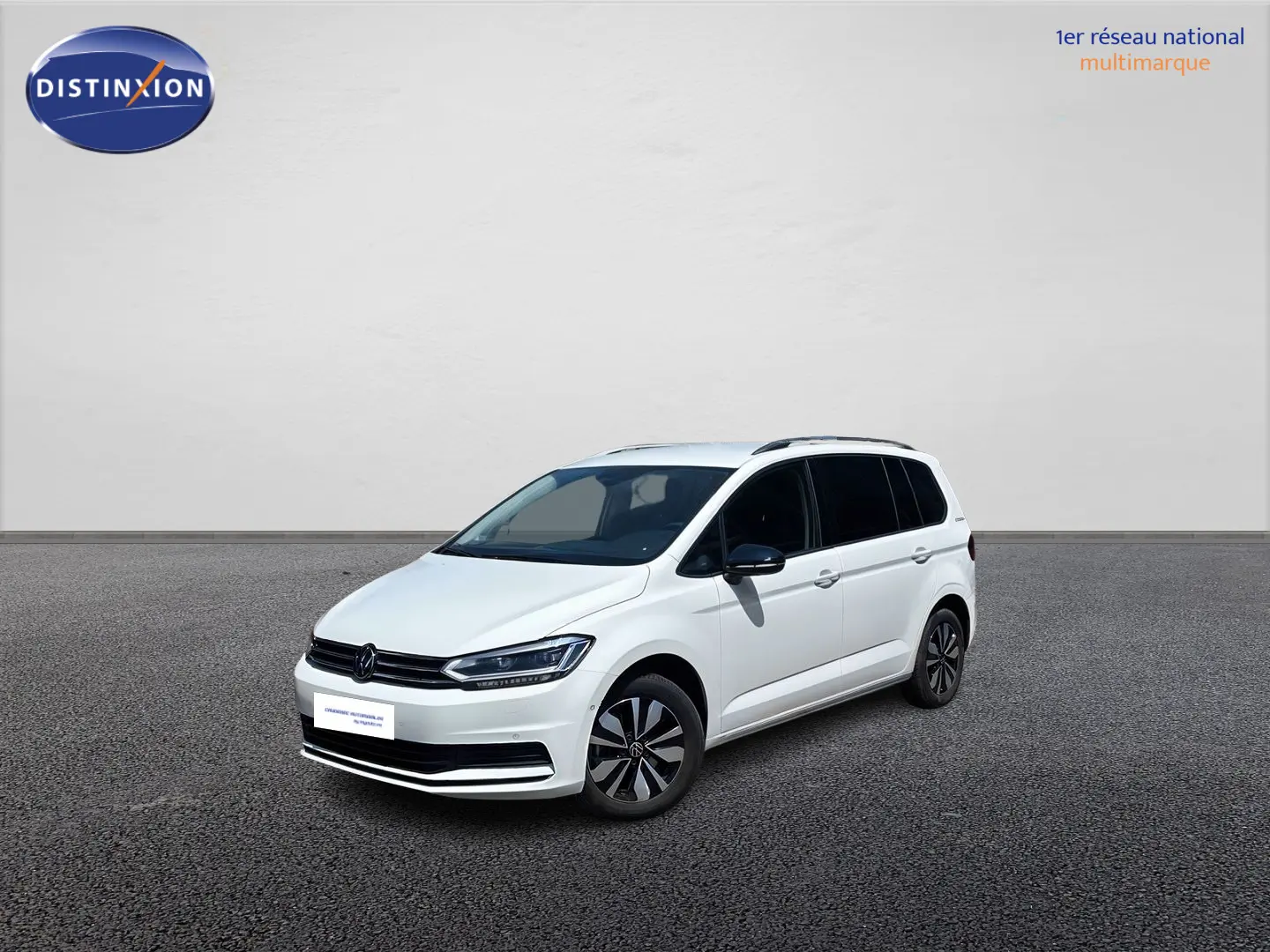 Volkswagen Touran blanc vue 3/4 avant droit, avec jantes alliage et vitres arrière surteintées.