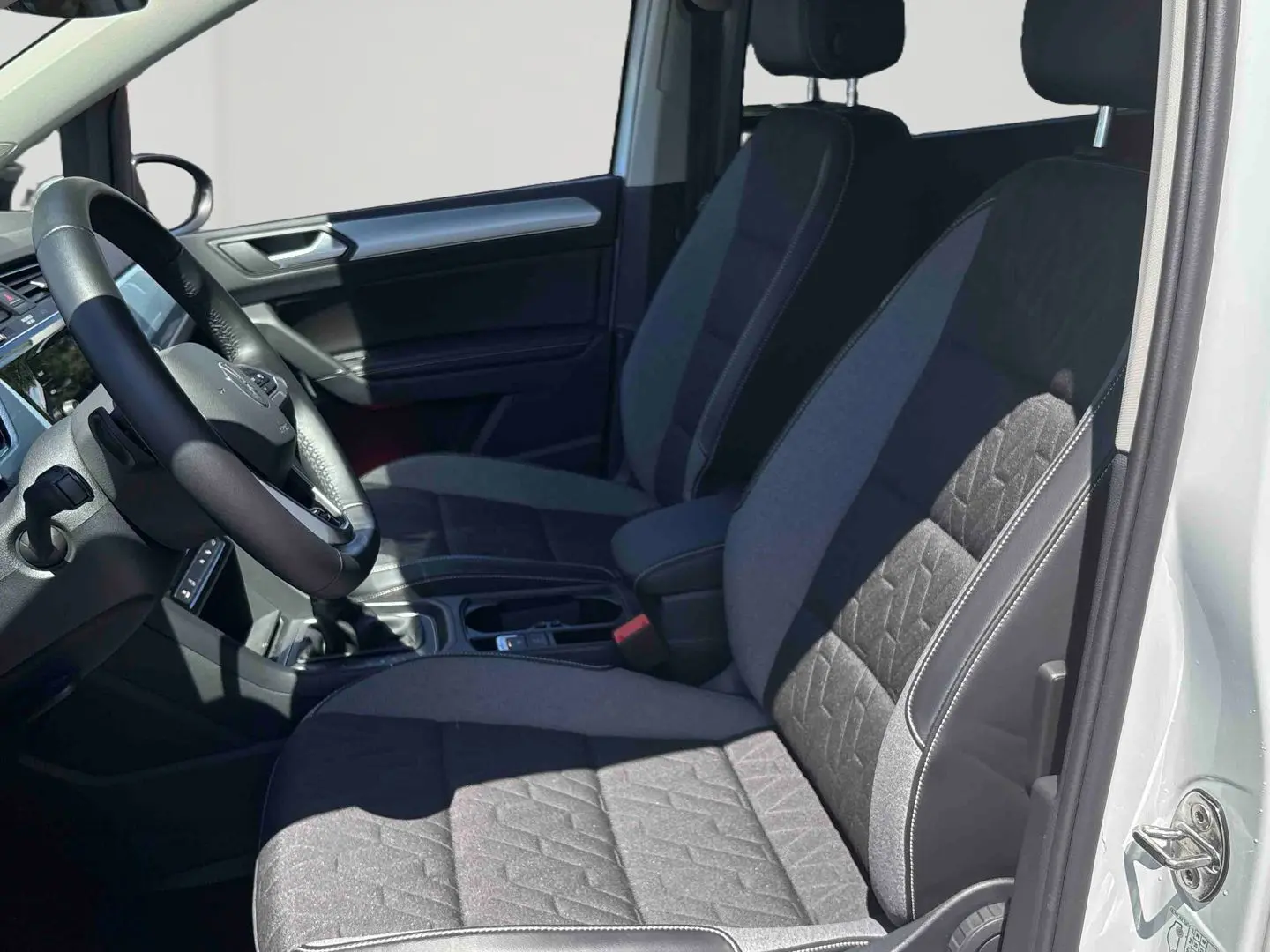 Vue intérieure côté conducteur du Volkswagen Touran 2025 avec sièges tissu gris et volant multifonctions en cuir.