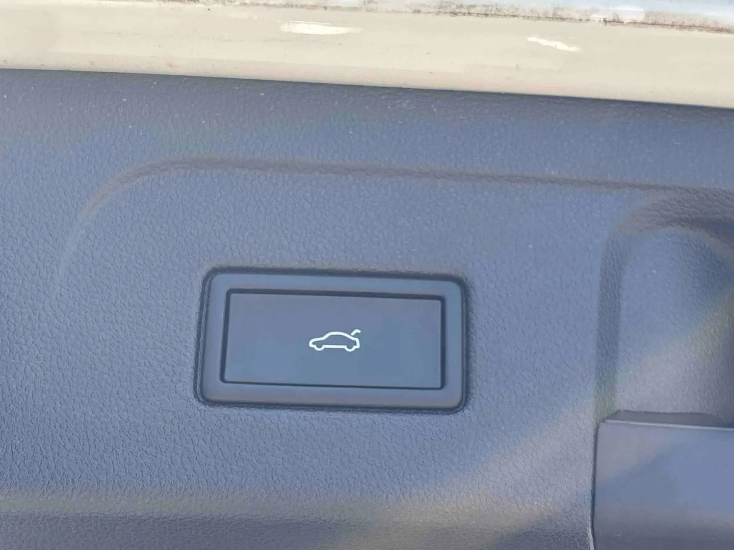 Bouton d'ouverture électrique du hayon sur la garniture intérieure du coffre du Volkswagen Touran blanc.