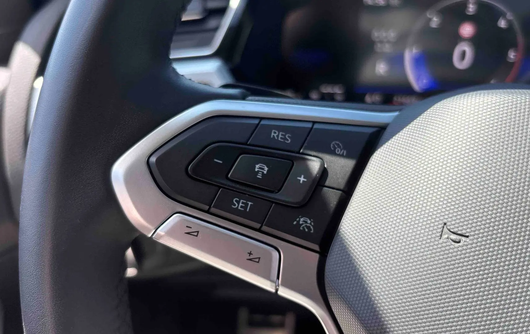 Gros plan sur les commandes du volant cuir multifonctions du Volkswagen Touran blanc, avec régulateur adaptatif et assistant de maintien de voie.