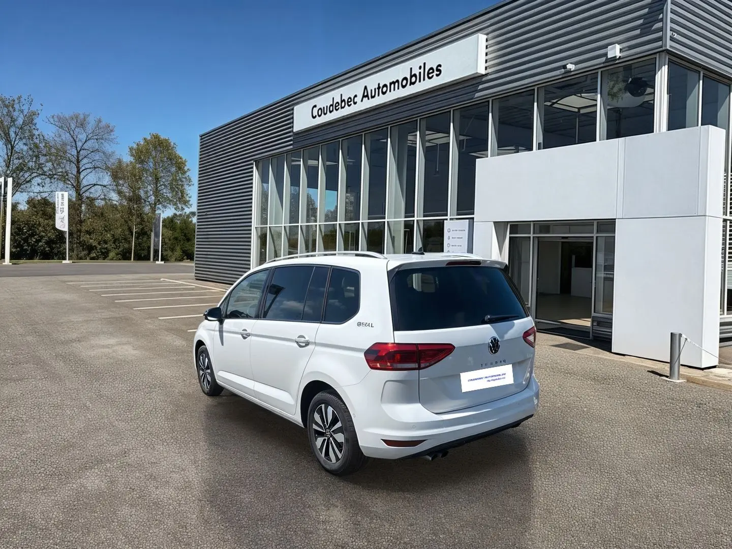 Volkswagen Touran blanc vue 3/4 arrière droit, stationné devant un bâtiment commercial moderne.