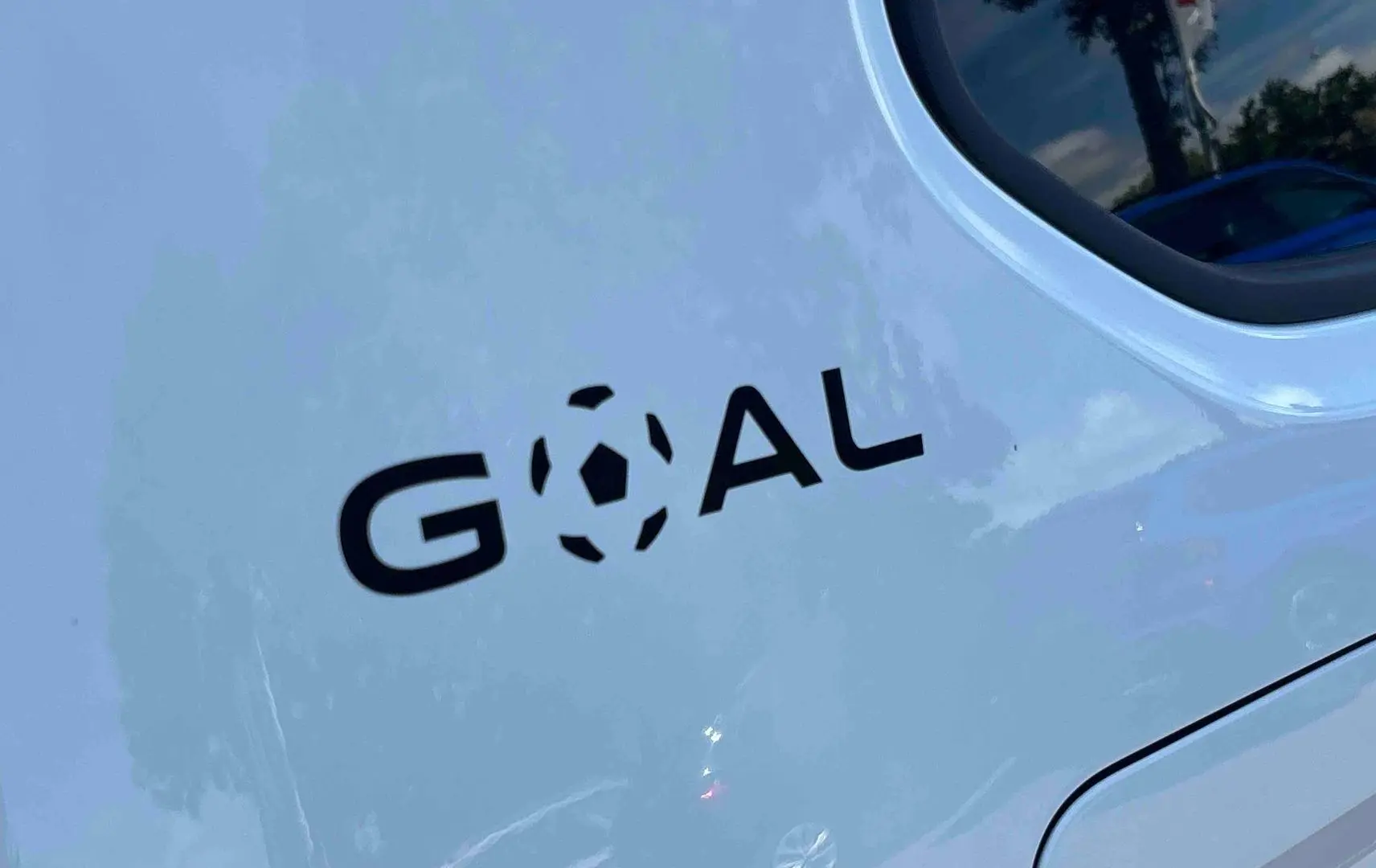 Détail du logo "GOAL" noir sur la porte arrière blanche d’un Volkswagen Touran 2025, vue latérale droite.