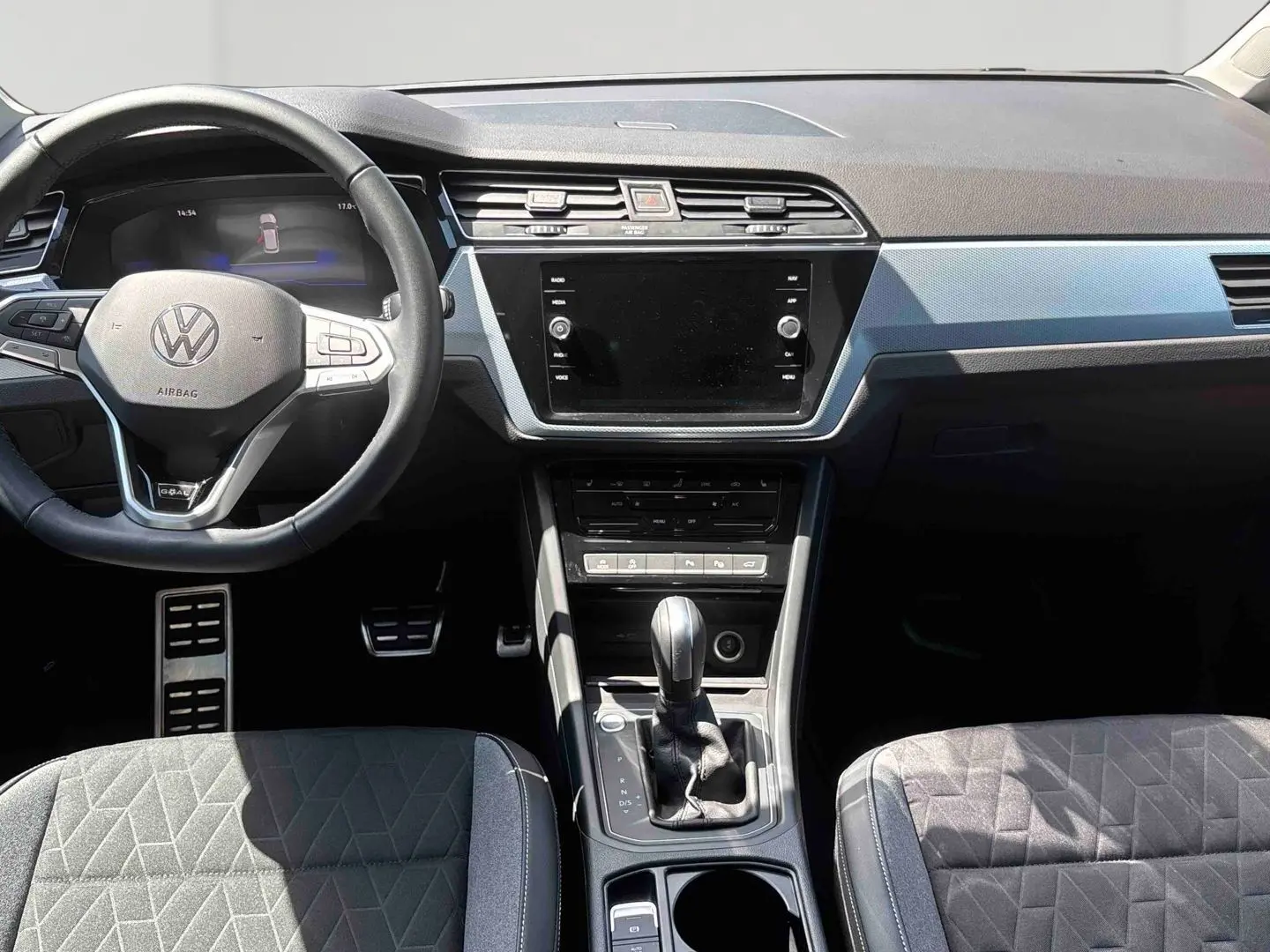 Vue intérieure frontale du tableau de bord et volant cuir noir du Volkswagen Touran blanc avec levier de vitesses manuel.