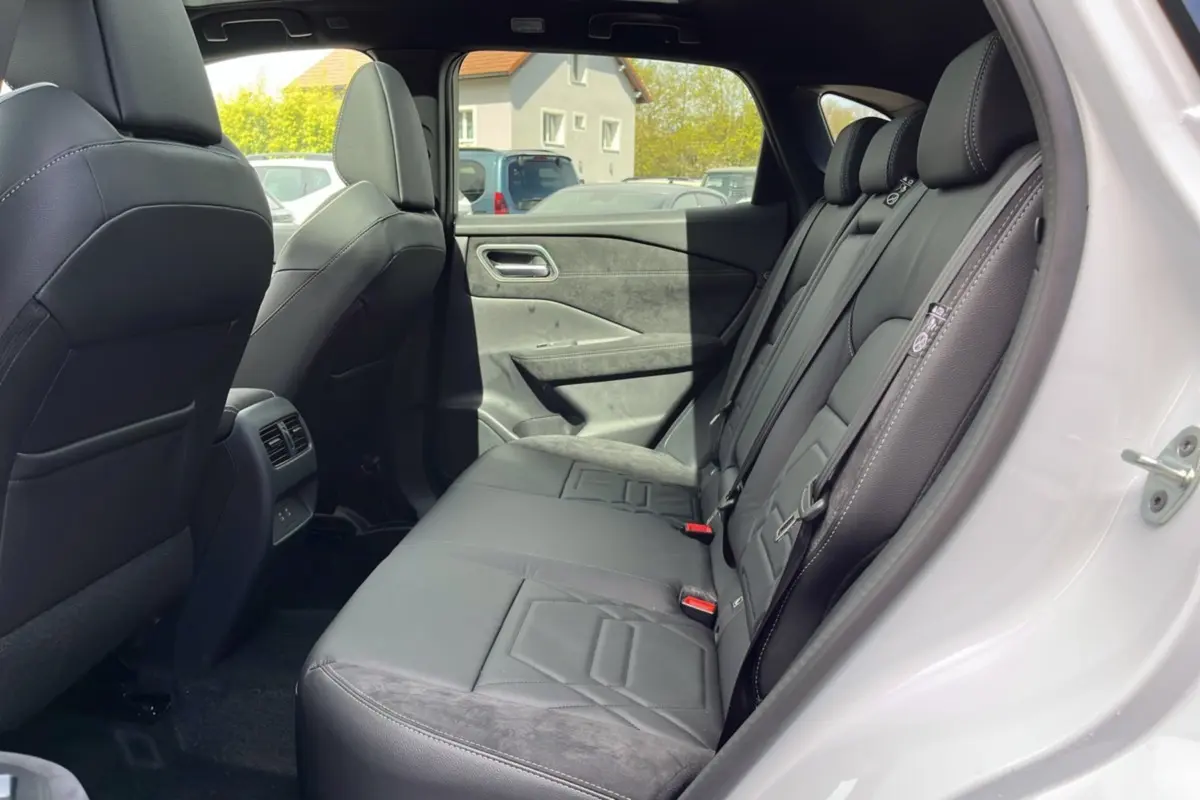 Vue côté droit de l’habitacle arrière du Nissan Qashqai blanc nacré, avec sellerie cuir alcantara noire et vitres surteintées.