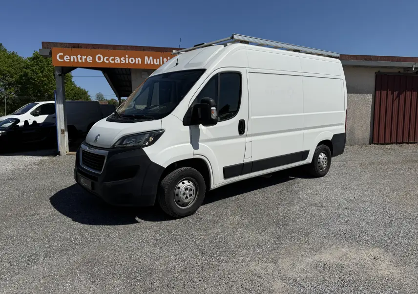 Fourgon Peugeot Boxer blanc vu de trois quarts avant droit, avec toit surélevé et protections noires sur les bas de caisse.
