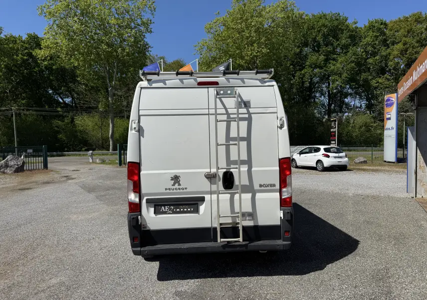 Vue arrière d'un Peugeot Boxer Fourgon blanc 2019 avec échelle fixée sur la porte et galerie sur le toit.