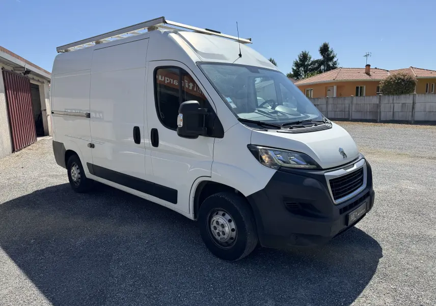 Fourgon Peugeot Boxer blanc vu en 3/4 avant droit, avec galerie de toit et pare-chocs noirs visibles.