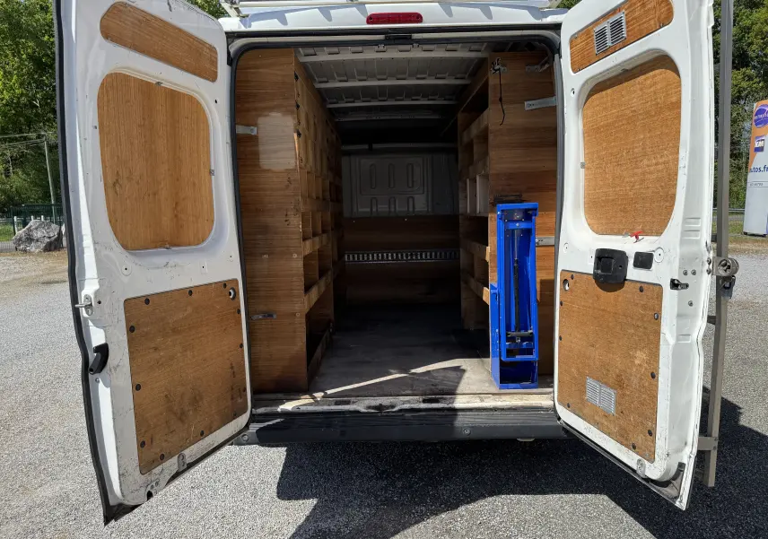 Vue arrière du Peugeot Boxer Fourgon blanc 2019 avec portes ouvertes révélant un aménagement intérieur en bois et un outil bleu.