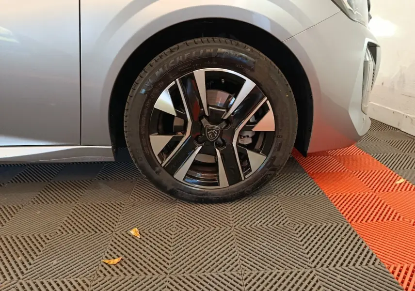 Gros plan sur la roue avant gauche d'une Peugeot 208 gris clair avec jante noire et argentée au design moderne