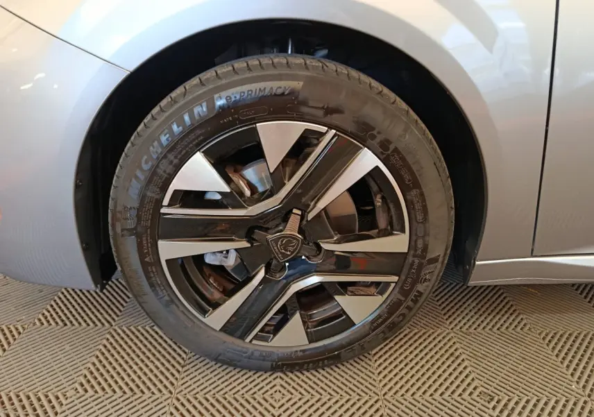 Gros plan sur la roue avant gauche gris clair d'une Peugeot 208 PureTech 100 S&S Allure avec jante noire et argent.
