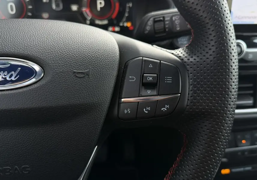 Gros plan sur le volant perforé noir avec commandes intégrées et tableau de bord numérique du Ford Puma 2024.