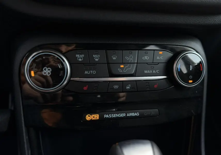 Gros plan sur la console centrale du Ford Puma gris magnétique, avec commandes climatisation et sièges chauffants allumés.