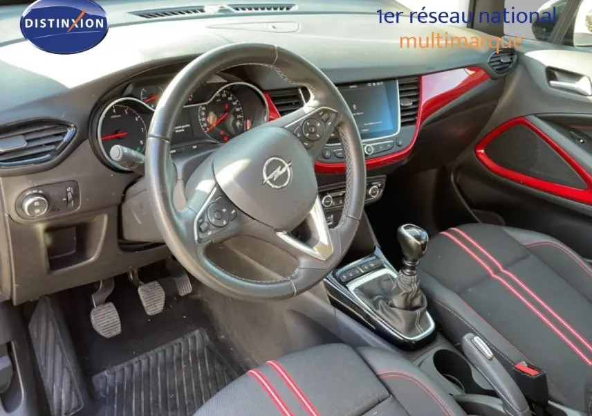 Vue intérieure côté conducteur de l’Opel Crossland 2023, volant cuir, tableau de bord noir avec inserts rouges et levier de vitesse manuel.