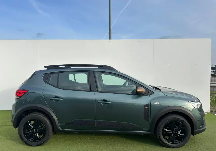 Profil droit de la Dacia Sandero Stepway 2025 en Vert Cèdre avec jantes noires et barres de toit brun cuivré.
