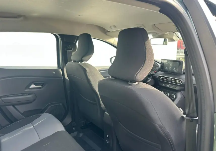 Vue intérieure arrière droite de la Dacia Sandero III Stepway, sièges noirs et tableau de bord avec écran tactile visible.