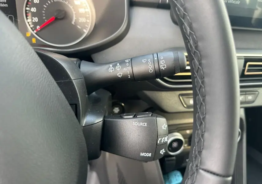 Gros plan sur la commande multimédia et le commodo d’essuie-glace côté gauche du volant d’une Dacia Sandero III Stepway.