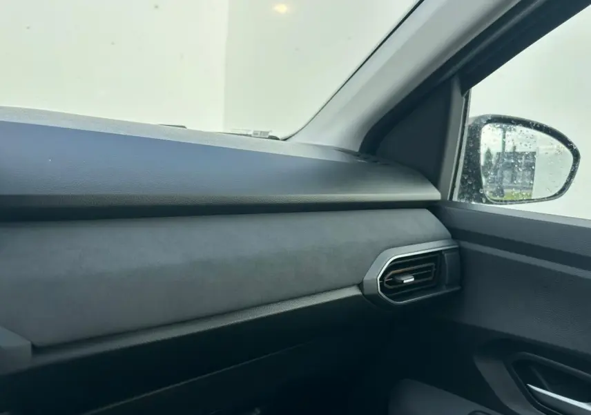 Intérieur côté passager de la Dacia Sandero III Stepway 2025, tableau de bord gris et sortie d'air hexagonale.