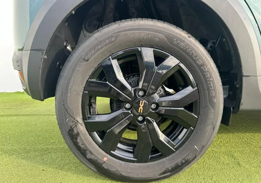 Gros plan sur la roue avant droite avec jante aluminium noire brillante du Dacia Sandero Stepway Vert Cèdre 2025.