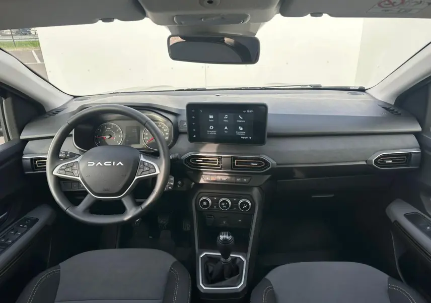Vue intérieure avant du tableau de bord de la Dacia Sandero III Stepway avec écran tactile et volant noir.