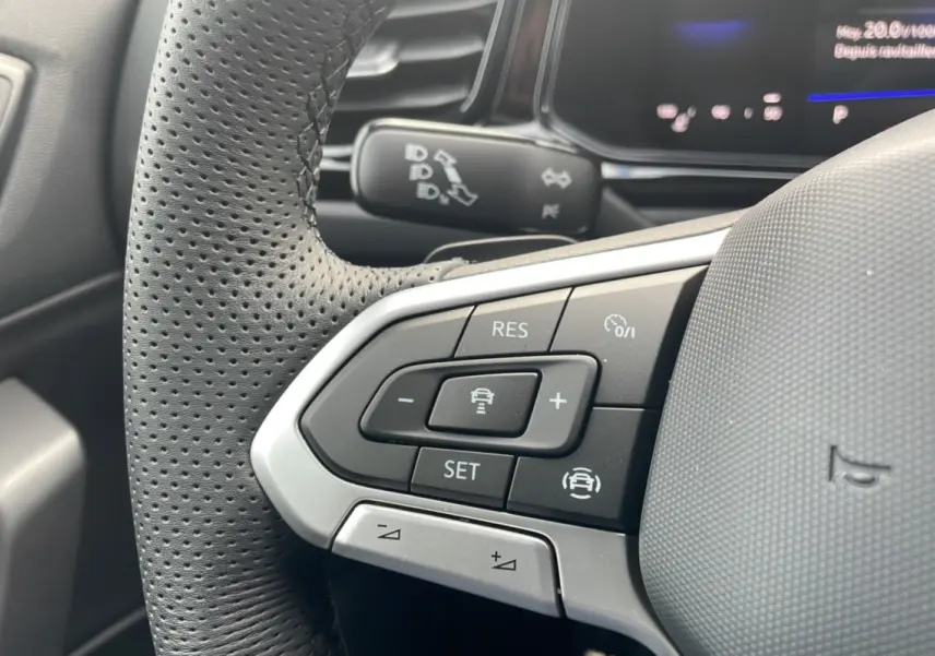 Gros plan sur le volant cuir noir perforé du Volkswagen T-Roc 2025, boutons multifonctions et commandes de régulateur visibles.