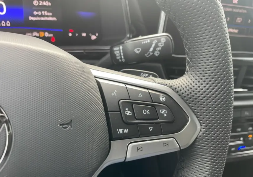 Gros plan sur le volant cuir perforé du Volkswagen T-Roc 2025 avec commandes multifonctions et affichage digital en arrière-plan.