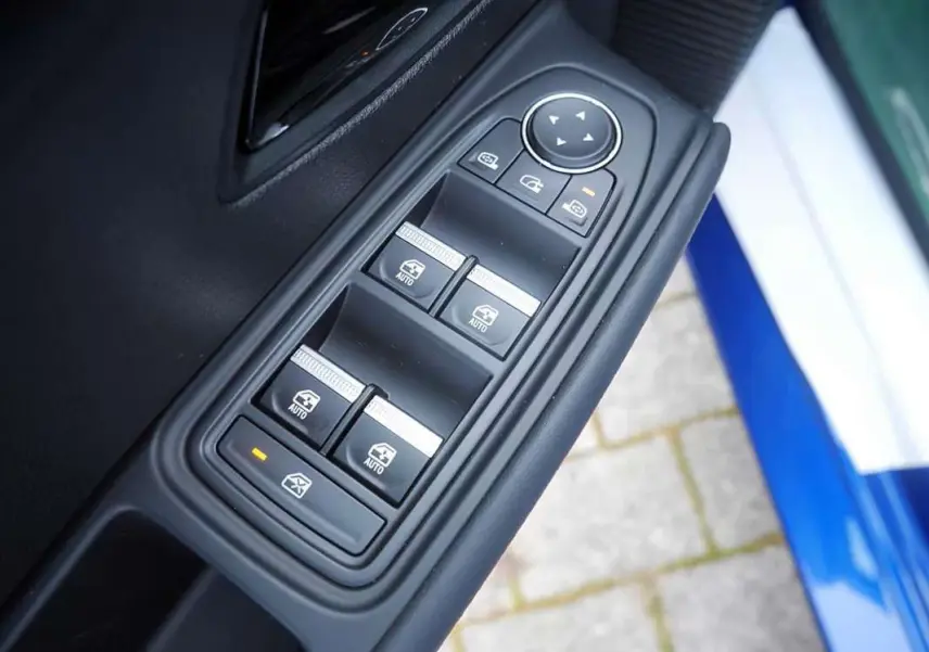 Gros plan sur les commandes des vitres électriques côté conducteur de la Renault Clio VI bleu iron, porte ouverte.