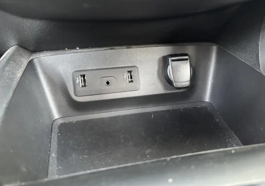 Gros plan sur la prise USB double et prise 12V dans le compartiment de rangement intérieur du Renault Kadjar gris foncé.