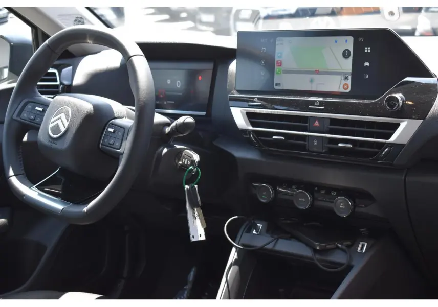 Vue intérieure côté conducteur du tableau de bord noir de la Citroën C4 Hybride 2025 avec écran tactile central et volant multifonction.