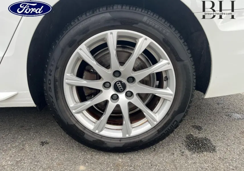 Gros plan sur la jante alu argentée avec logo Audi d'une roue arrière droite d'Audi A4 Avant blanc glacier métallisé.