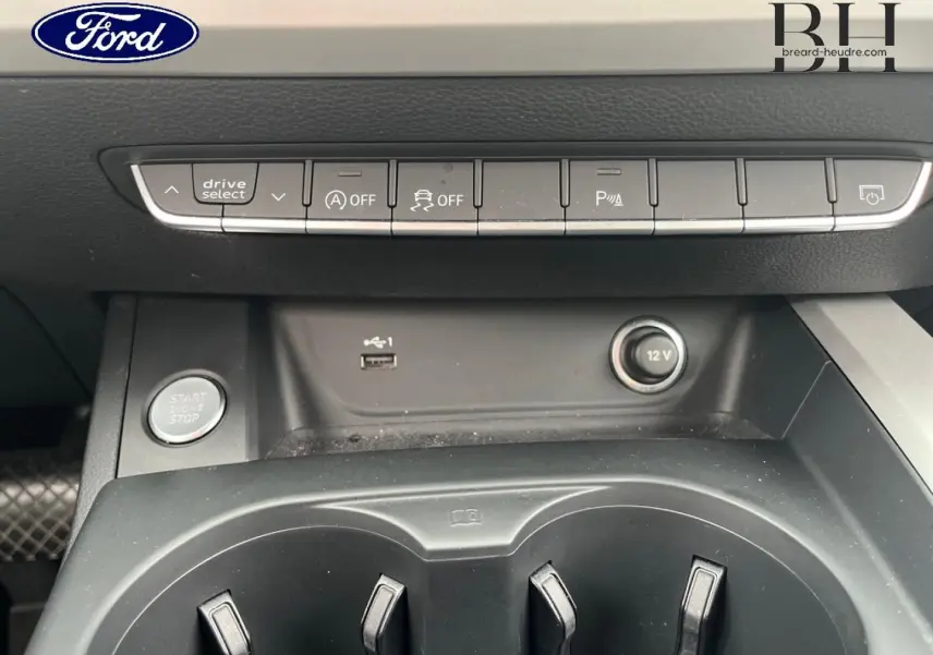 Vue rapprochée de la console centrale noire d'une Audi A4 Avant blanche, montrant les boutons de contrôle et prises USB et 12V.