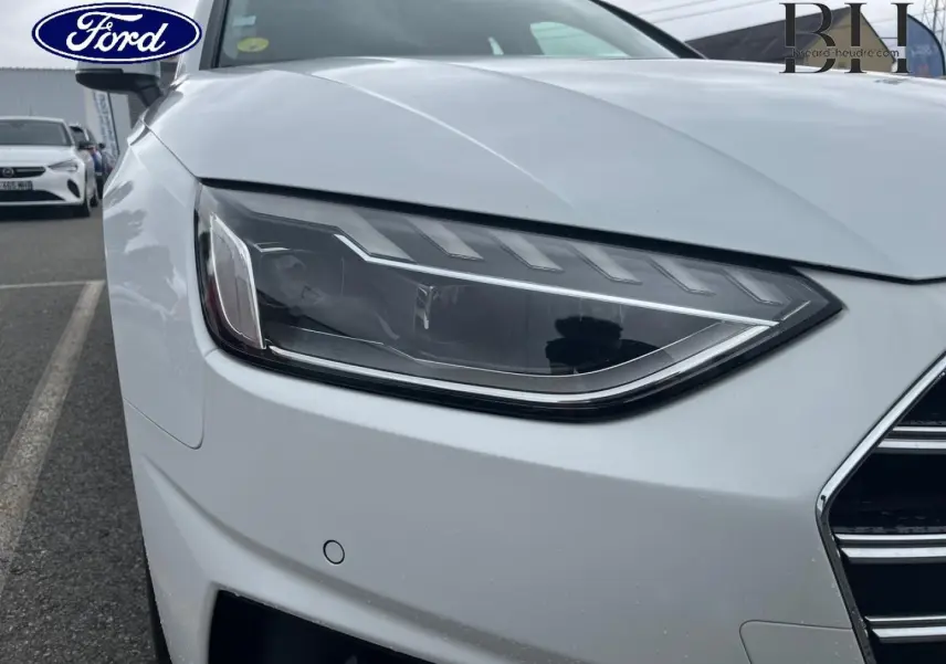 Gros plan sur le phare avant gauche d'une Audi A4 Avant blanc glacier métallisé, avec calandre partielle visible.