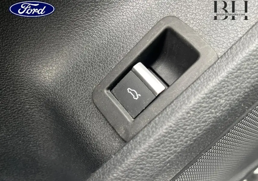 Bouton d'ouverture du coffre sur panneau intérieur noir, détail d'une Audi A4 Avant blanc glacier métallisé 2021.