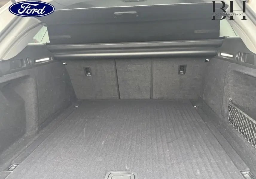 Coffre ouvert d'Audi A4 Avant blanc glacier, vue intérieure arrière montrant un espace de chargement spacieux et tapis noir.
