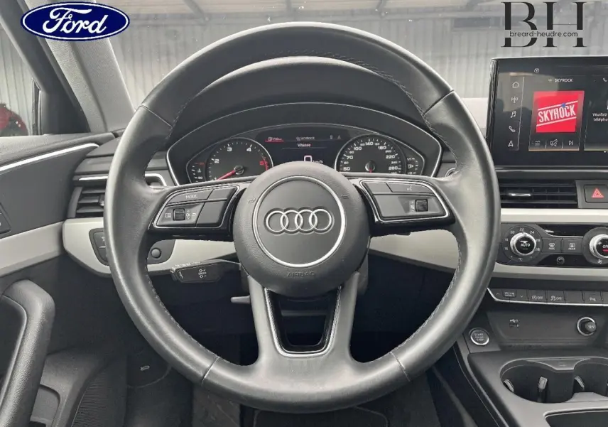 Vue intérieure centrée sur le volant cuir Audi avec tableau de bord et écran multimédia en arrière-plan.